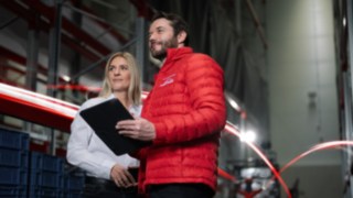 myLinde puede adaptarse de forma flexible a las necesidades de su empresa. Un hombre con una chaqueta roja Linde MH y una mujer con una camisa blanca están de pie en un almacén y miran de lejos.
