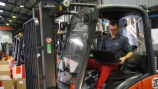 El técnico realiza la inspección de una carretilla usada Técnico con ordenador portátil durante la inspección de una carretilla para el reacondicionamiento