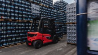 La carretilla eléctrica Linde X30 transporta cajas de bebidas por un estrecho pasillo del almacén exterior.