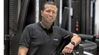 Tibor Sevenheck se apoya en una carretilla de pasillo estrecho (VNA) y sonríe a la cámara.