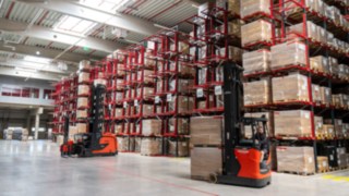 Carretillas de pasillo estrecho (VNA) y carretillas retráctiles de Linde frente a una estantería de palés