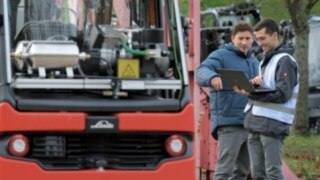 Los vehículos autónomos deben ser tan atentos, receptivos y proactivos como los conductores humanos de carretillas elevadoras. Dos hombres se colocan delante de una carretilla elevadora autónoma y miran juntos los datos del ordenador portátil.