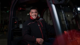 Un empleado de Linde Material Handling está sentado en un vehículo de manutención y sonríe a la cámara.