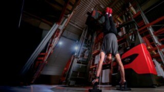 Un hombre vestido con ropa deportiva hace el pino junto a un vehículo de Linde MH.