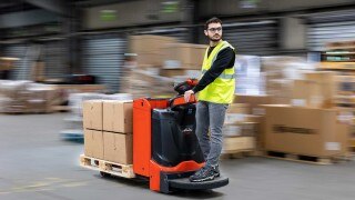 El Linde e-driver permite a los conductores controlar todas las funciones de la carretilla elevadora con una sola mano sin forzar la columna vertebral. Una transpaleta Linde T20 circula por un almacén, el conductor se sitúa en un ángulo de 45 grados